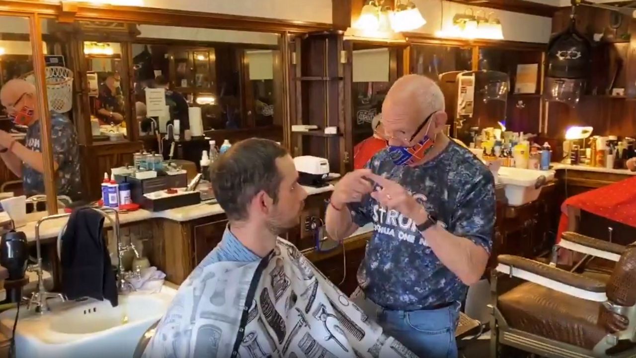 Earl Brigham, 75, gestures to customer Stephen Pyles at the barbershop that bears his name in Winter Garden, where he's cut hair for 45 years. (Pete Reinwald/Spectrum News 13)