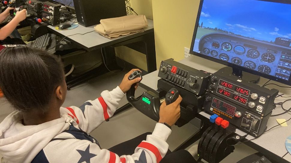 Girl dressed in a red white and blue hoodie with blue stars using the steering wheel on a simulator