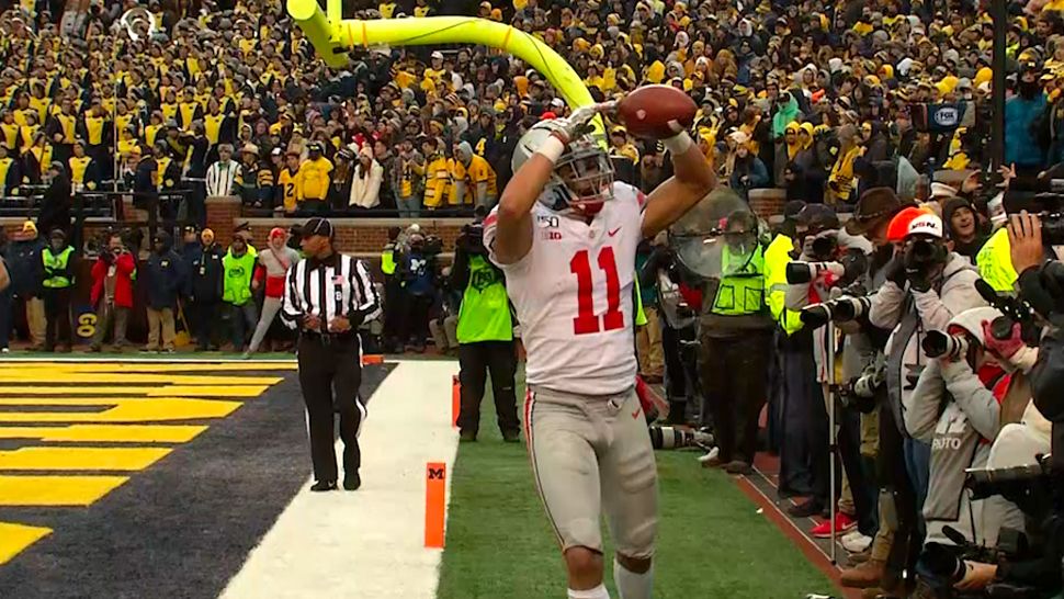 Ohio State Buckeyes Player Number 11 on the field holding a football with his hands up celebrating