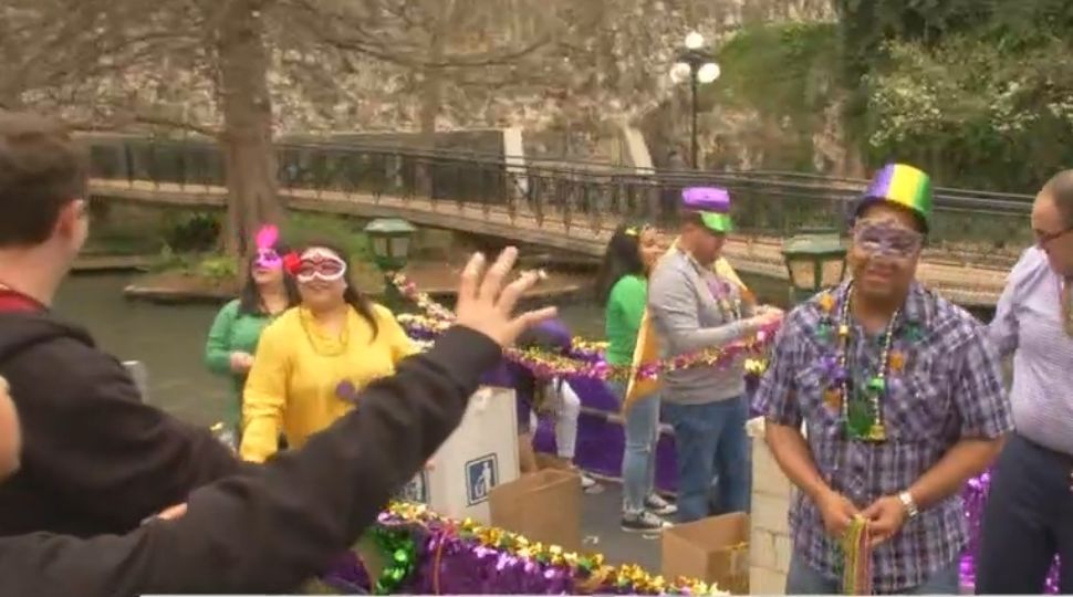 Boats of people hand out beads to people on San Antonio River Walk March 2, 2019 (Spectrum News)