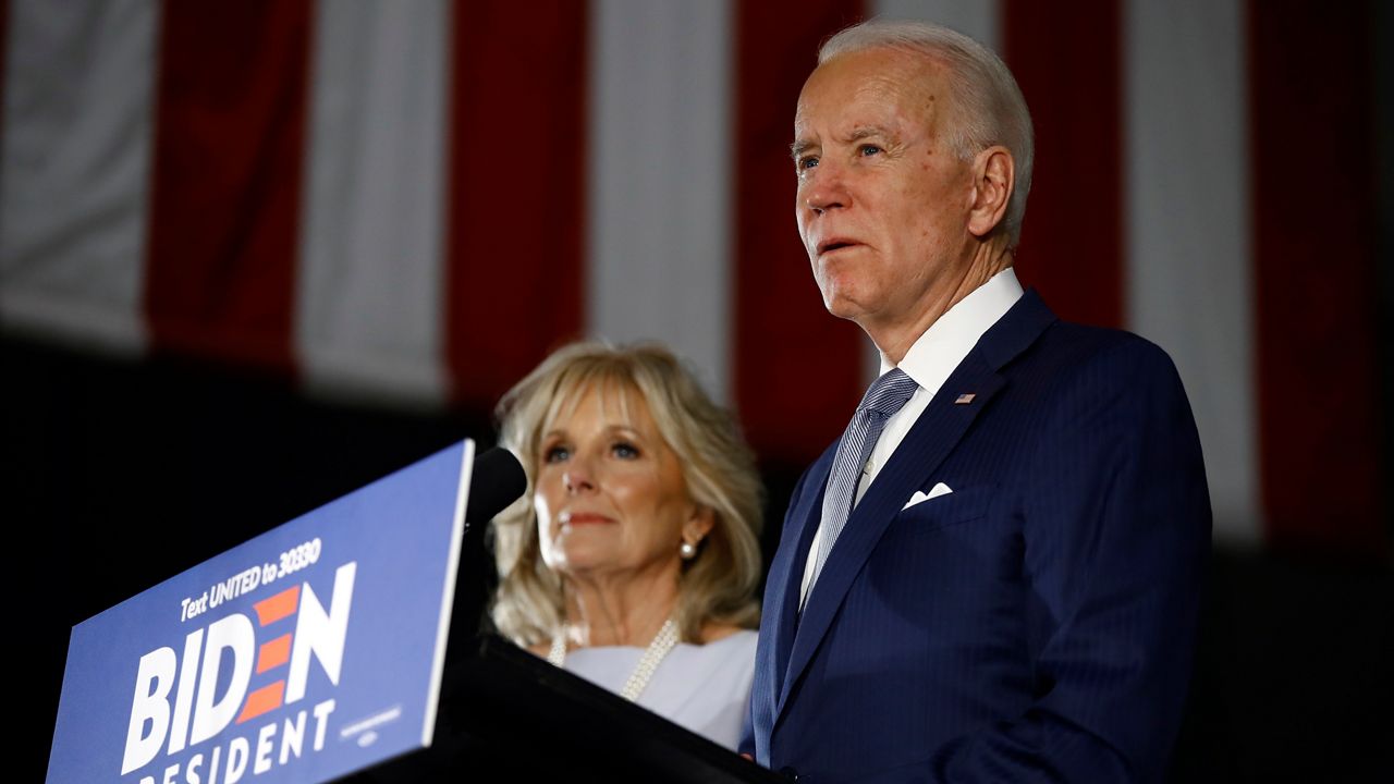 Joe Biden, right, wearing a navy blue suit jacket, a white dress shirt, and a silver tie, accompanied by his wife Jill, left, speaks at a lectern at the National Constitution Center in Philadelphia.