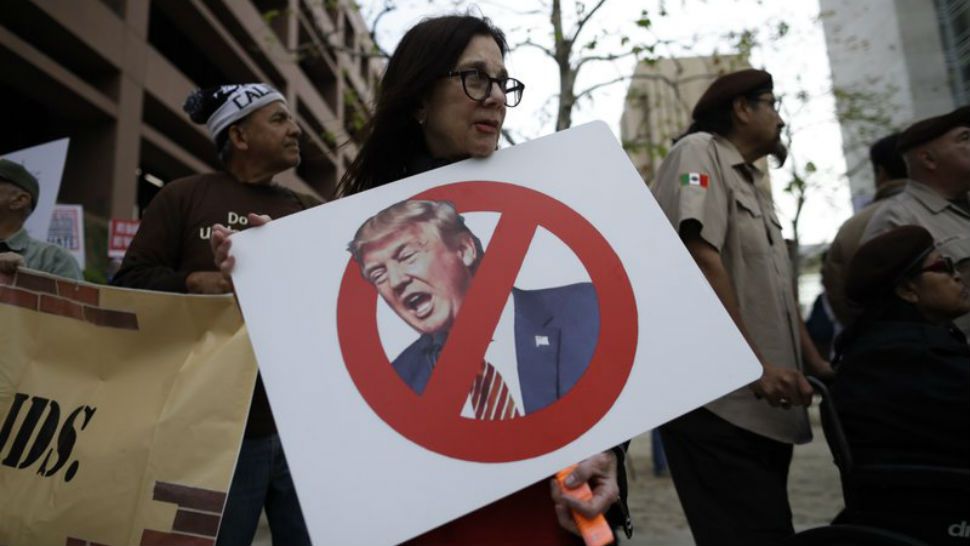 Jill Green holds a sign during a rally against a scheduled upcoming visit by President Donald Trump, Monday, March 12, 2018, in San Diego. Trump is scheduled to visit San Diego, Tuesday, setting foot in California for his first time as president. (AP Photo/Gregory Bull)