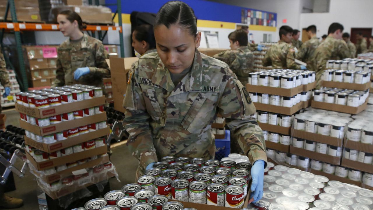 Specialist Yadira Izaguirre of the California National Guard picks up case of soup that will be packed with other food stuff supplies at the Sacramento Food Bank and Family Services in Sacramento, Calif., Saturday, March 21, 2020. Food banks have been hit hard by a shortage of volunteers due to the mandatory stay-at-home order caused by the coronavirus. Izaguirre and other members of the 115th Regional Support Group are supplementing food bank staff to ensure the food bank continues provide food to those in need. (AP Photo/Rich Pedroncelli)