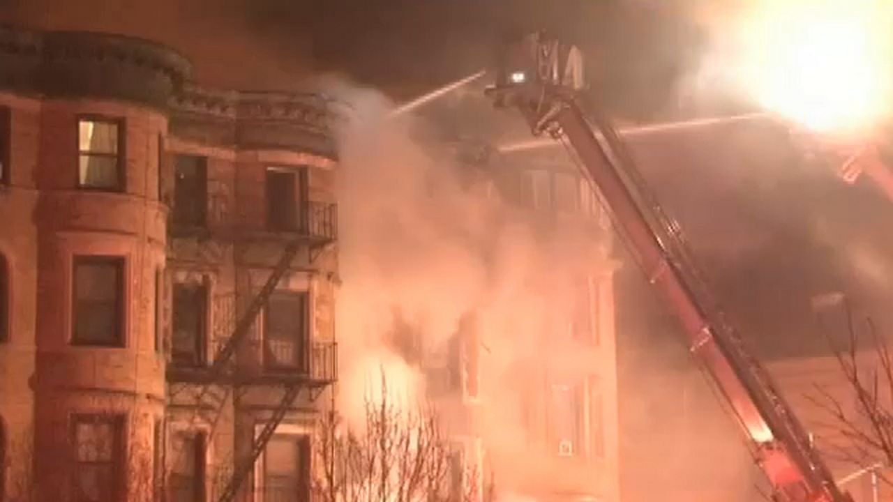 White smoke plumes from a building. Water is spread from the top of a ladder.