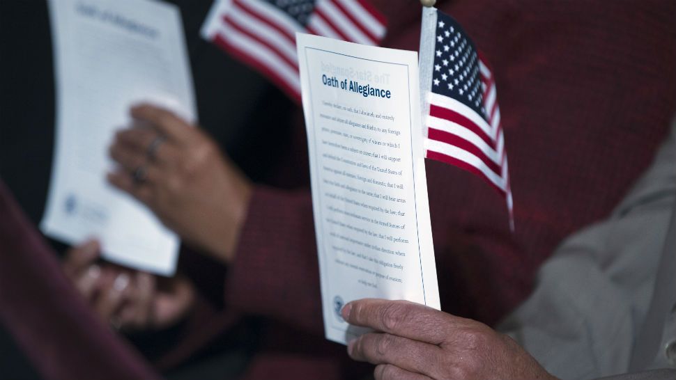 FILE- In this Dec. 15, 2015 file photo, participants hold the "Oath of Allegiance" and American flags during a naturalization ceremony attended by President Barack Obama at the National Archives in Washington. (AP Photo/Evan Vucci, File)