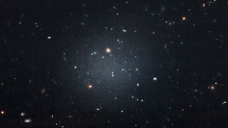 This Nov. 16, 2017 image made with the Hubble Space Telescope shows the diffuse galaxy NGC 1052-DF2, lighter area in center. Several other galaxies can be seen through it. The unusual galaxy's stars are speeding around with no apparent influence from dark matter, according to a study published on Wednesday, March 28, 2018 in the journal Nature. (P van Dokkum/NASA/ESA via AP)