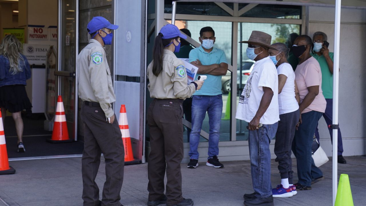 People wait to get their body temperature checked before getting in to get their vaccine at the Baldwin Hills Crenshaw Plaza in Los Angeles Thursday, April 1, 2021. (AP Photo/Damian Dovarganes)