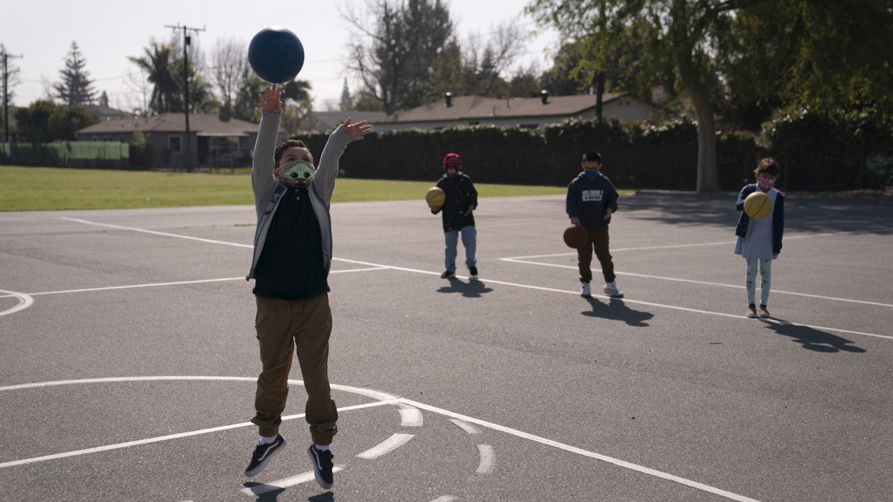 Third grader Matthew Egoavil shoots a ball on a basketball court as his socially distanced classmates wait for their turns at West Orange Elementary School in Orange, Calif. (AP Photo/Jae C. Hong)