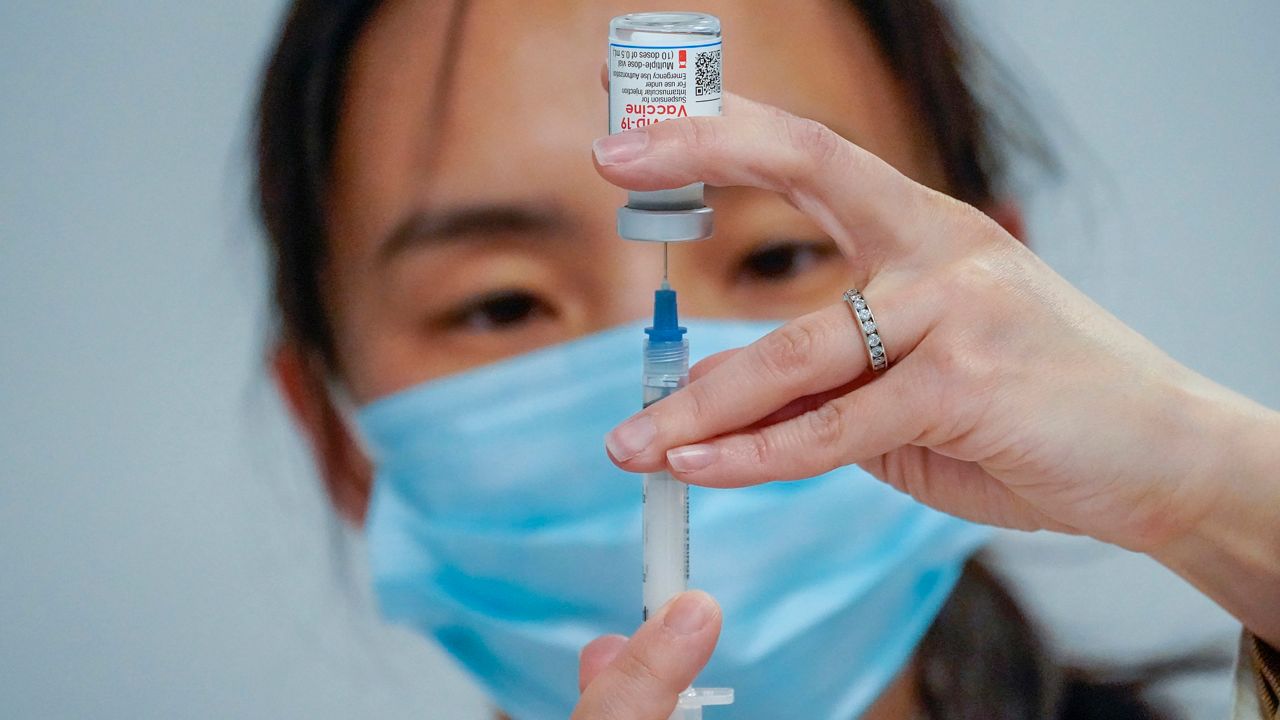 A pharmacist fills a syringe with Moderna's COVID-19 vaccine