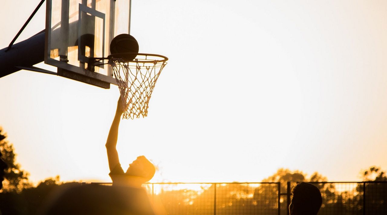 A generic image of a person shooting a layup on a basketball rim while the sun sets (Stock image)
