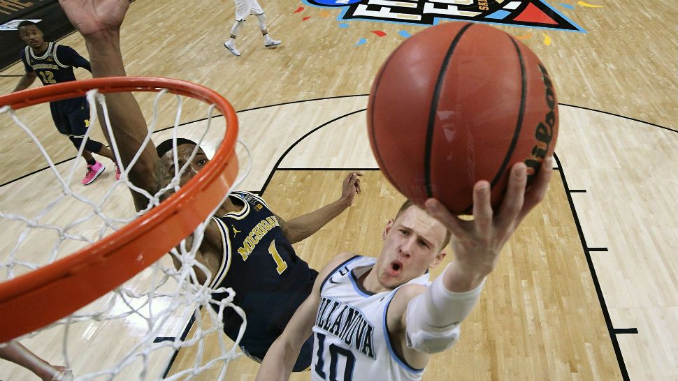 A Villanova player dunk the basketball in front of a Michigan player. 