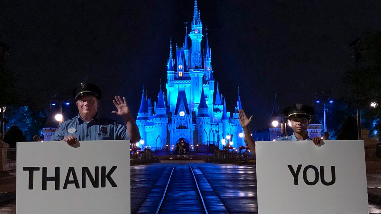 Disney World Resort security Cast Members Jack Cooper (left) and Branland Vaughn (right) hold “thank you” signs for medical workers while standing in front of Cinderella Castle at Magic Kingdom Park (Courtesy of Disney)