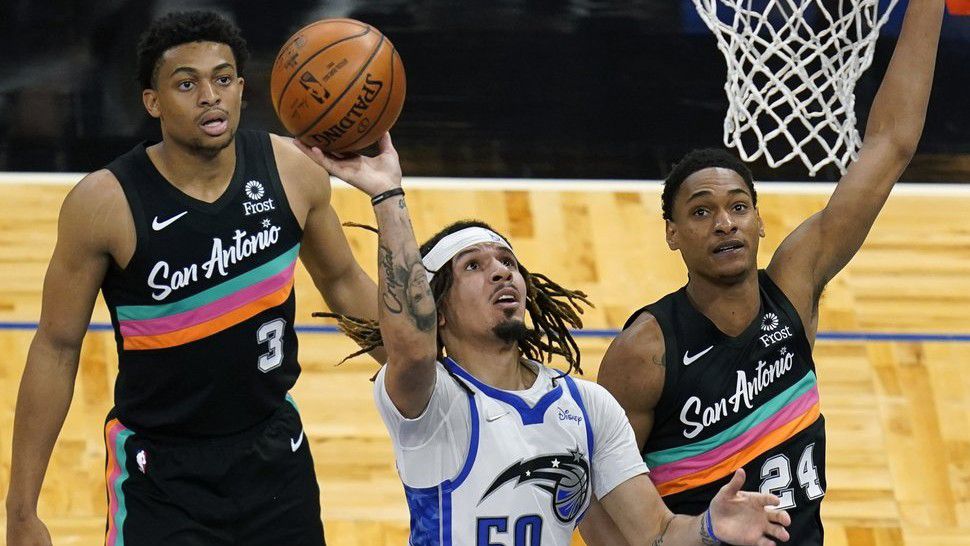 Orlando Magic guard Cole Anthony (50) takes a shot as he gets between San Antonio Spurs forward Keldon Johnson (3) and guard Devin Vassell (24) during the first half of an NBA basketball game, Monday, April 12, 2021, in Orlando, Fla. (AP Photo/John Raoux)