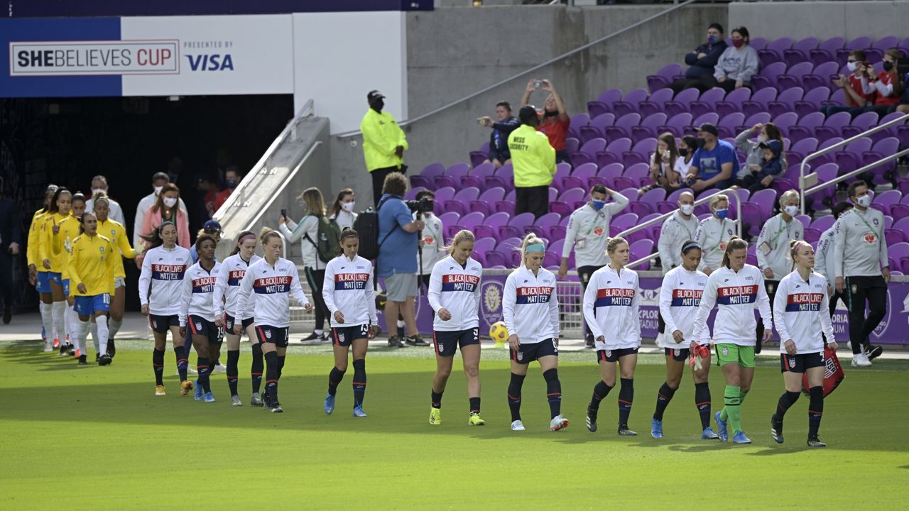 United States players wear jackets with a social awareness message on them as they enter the pitch before a SheBelieves Cup women's soccer match against Brazil, Sunday, Feb. 21, 2021, in Orlando, Fla. (AP Photo/Phelan M. Ebenhack)