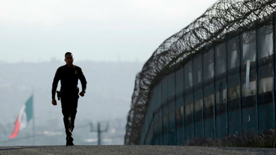 FILE - In this June 22, 2016 file photo, Border Patrol agent Eduardo Olmos walks near the secondary fence separating Tijuana, Mexico, background, and San Diego in San Diego. California has rejected the federal government’s initial plans for National Guard troops to the border because the work is considered too closely tied to immigration enforcement. (AP Photo/Gregory Bull, File)