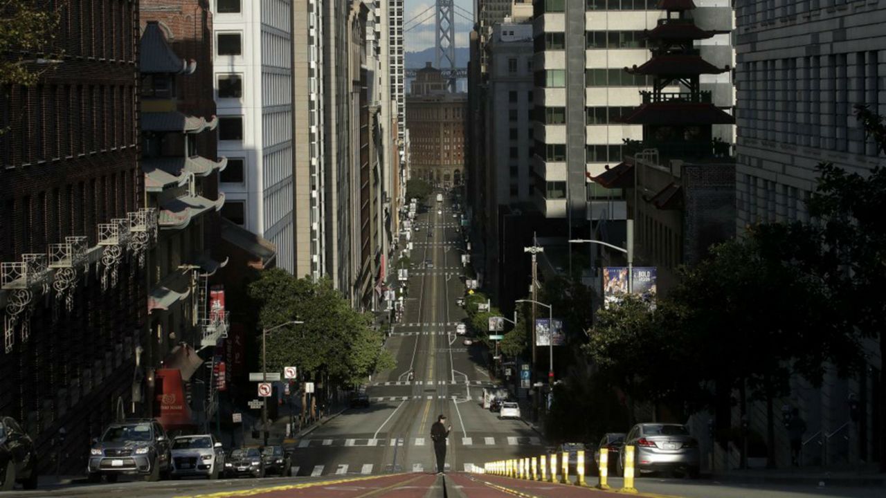 FILE - In this March 21, 2020, file photo, a man stands in the middle of a cable car tracks on a near empty California Street in San Francisco. On the morning of March 15, as Italy became the epicenter of the global coronavirus pandemic, a half dozen high-ranking California health officials held an emergency conference call to discuss a united effort to contain the spread of the virus in the San Francisco Bay Area. That call and the bold decisions that came in the hours afterward have helped California avoid the kind of devastation from the virus in parts of Europe and New York City. (AP Photo/Jeff Chiu, File)