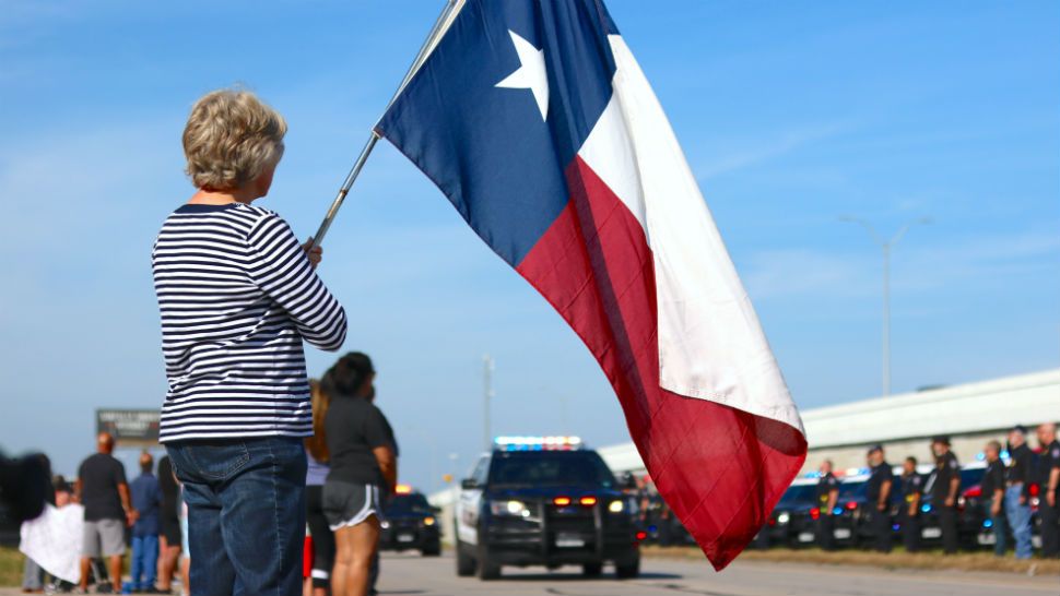 A woman holds the Texas flag during a procession for Justin Putnam. (Stacy Richard/Spectrum News)