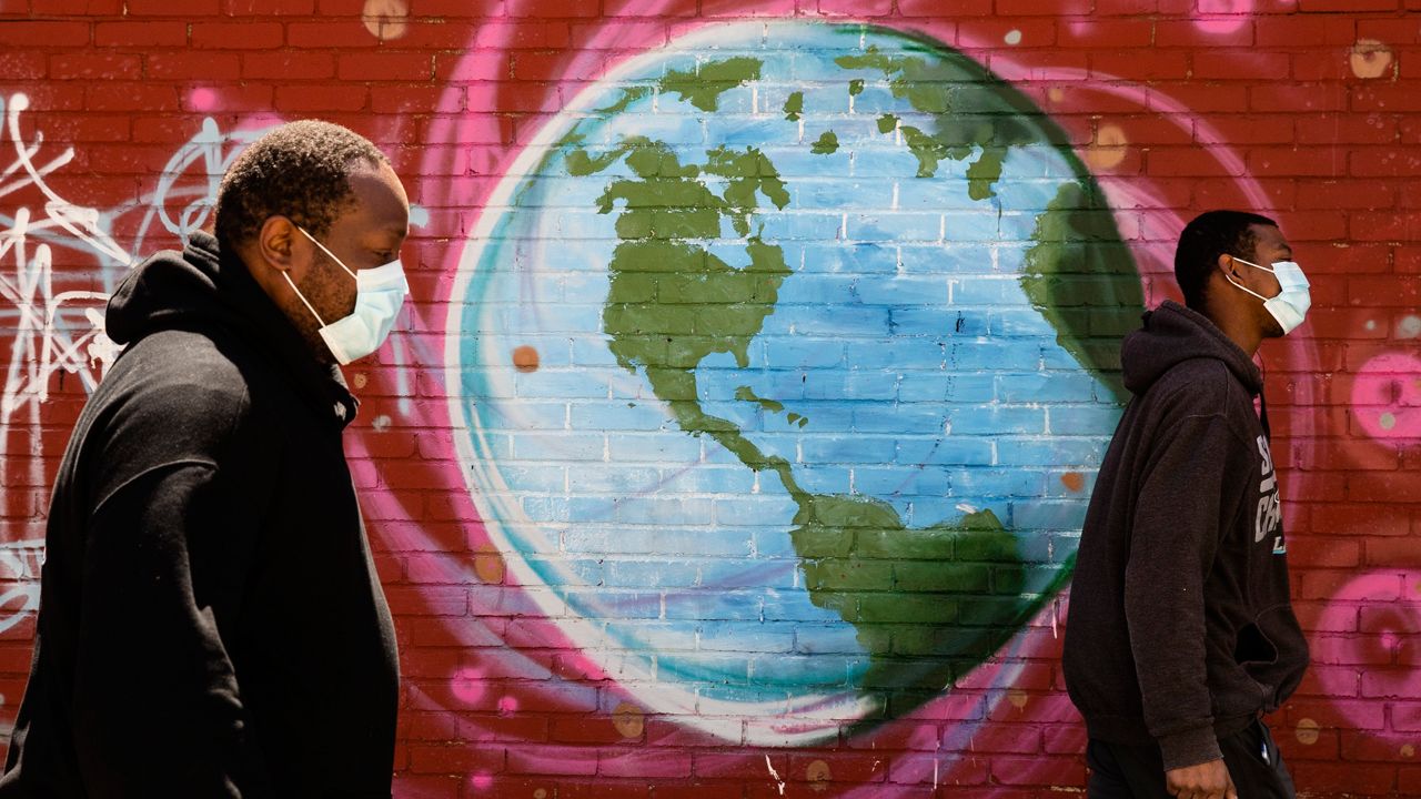 Two people in masks walk past a mural of the Earth