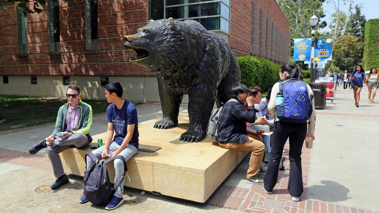 In this April 26, 2019, file photo, people stand next to the Bruin statue, the UCLA Mascot, Joe Bruin of the University of California, Los Angeles. (AP Photo/Reed Saxon)