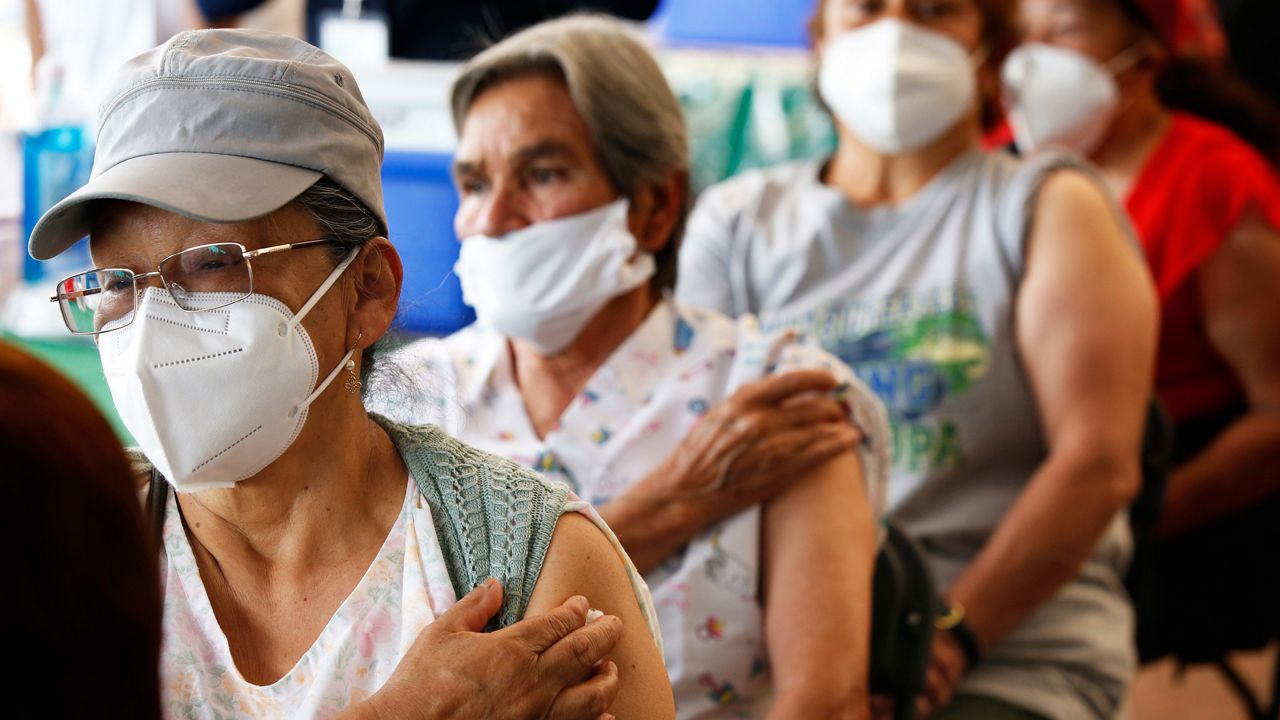Four people in masks wait after receiving a COVID-19 vaccine dose