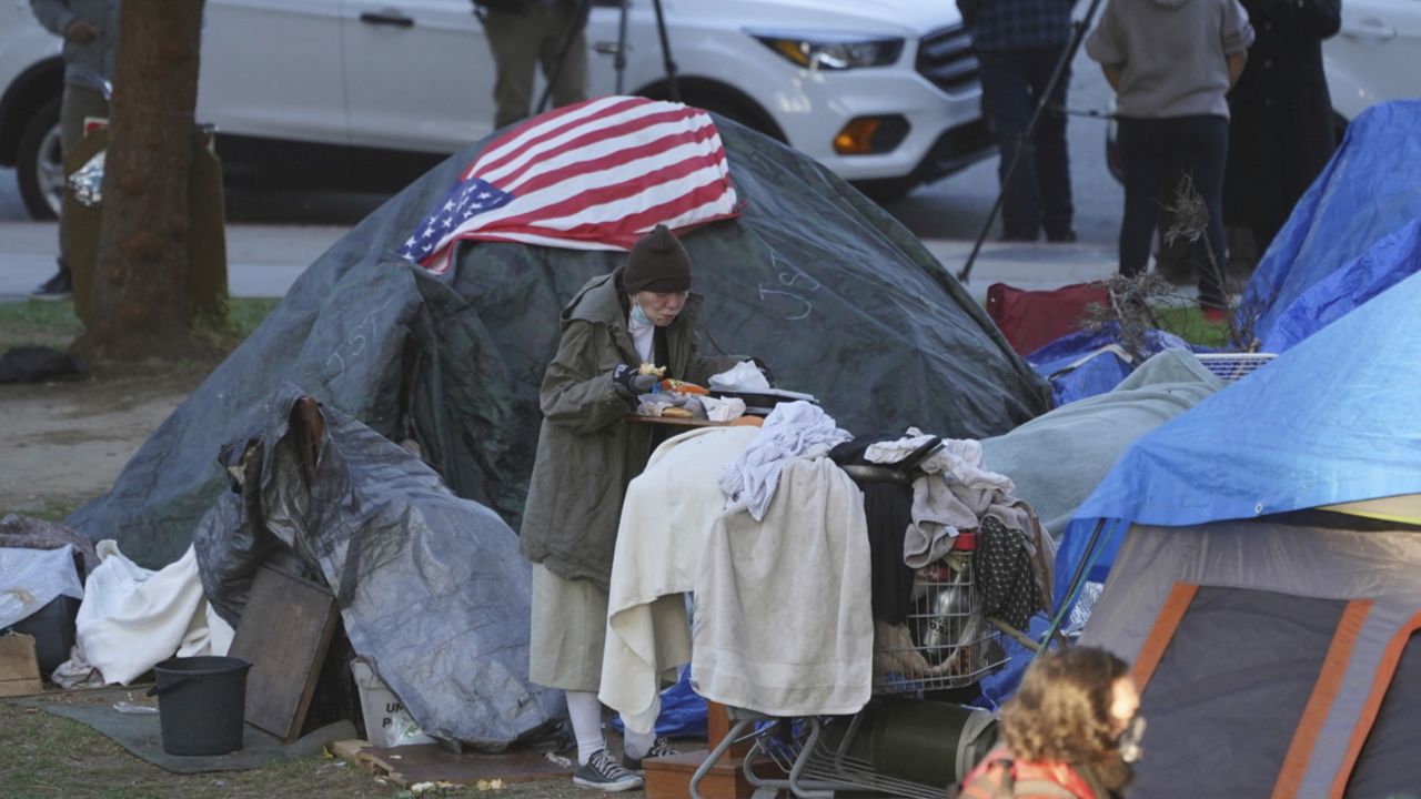 A woman eats at her tent at the Echo Park homeless encampment at Echo Park Lake in Los Angeles on March 24, 2021. (AP Photo/Damian Dovarganes)