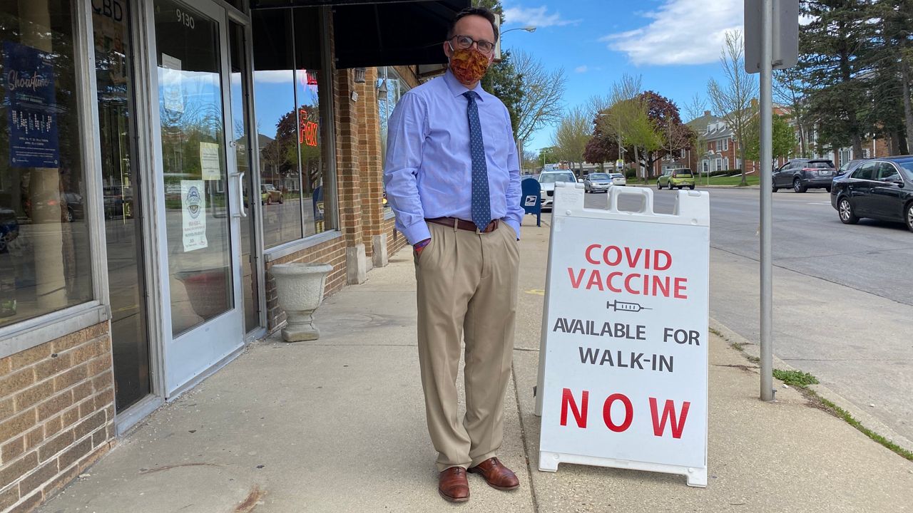 Pharmacist Randy Dawes stands next to a sign advertising walk-in COVID-19 vaccines