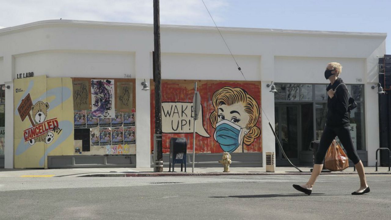 A masked pedestrian walks past a coronavirus-themed mural Monday, May 18, 2020, in the arts district of Los Angeles. (AP Photo/Marcio Jose Sanchez)