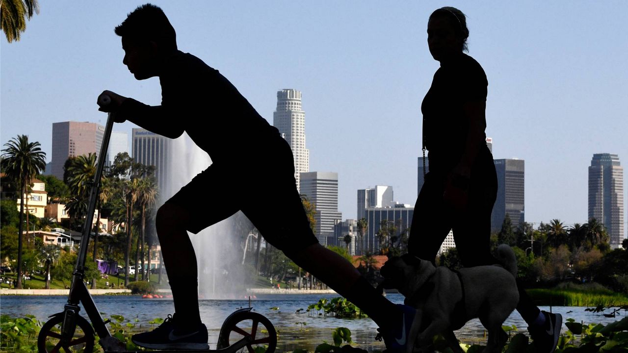 A young boy and a woman use the bike path at Echo Park Lake with downtown Los Angeles in the background Saturday, May 23, 2020. (AP Photo/Mark J. Terrill)