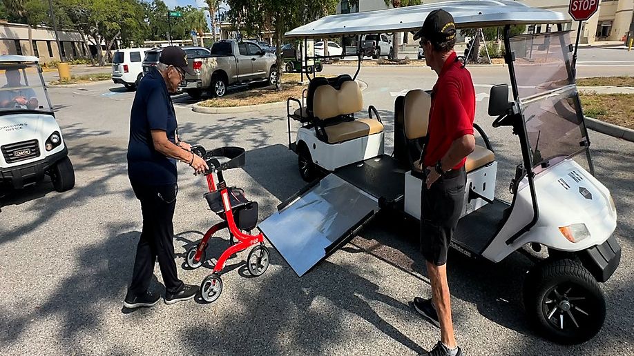 Ricky Glisson helps a veteran onto a golf cart to take him to another building. (Spectrum Bay News 9/Matt Lackritz)