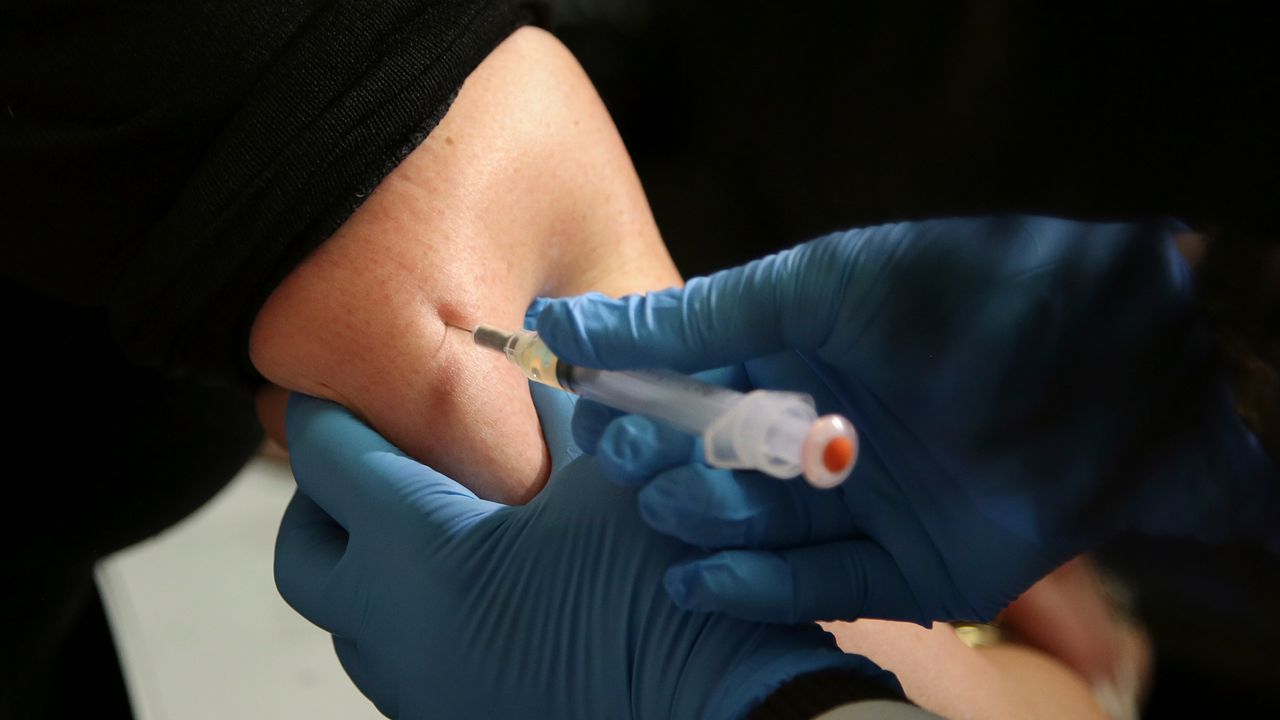 A person wearing a black shirt gets a shot from someone wearing blue gloves.
