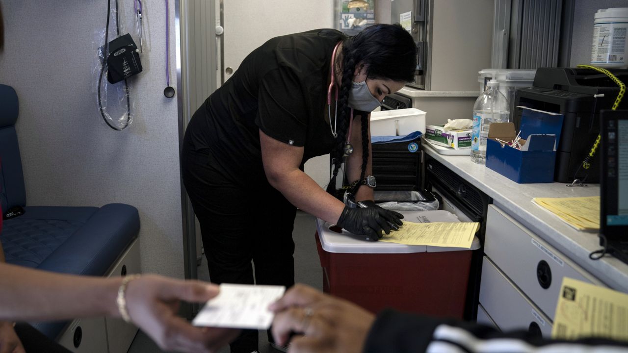Nurse Natasha Garcia does paperwork after administering a dose of the Moderna COVID-19 vaccine to Magaly Esparza, foreground left, at a mobile clinic set up in the parking lot of a shopping center in Orange, Calif., Thursday, April 29, 2021. (AP Photo/Jae C. Hong)