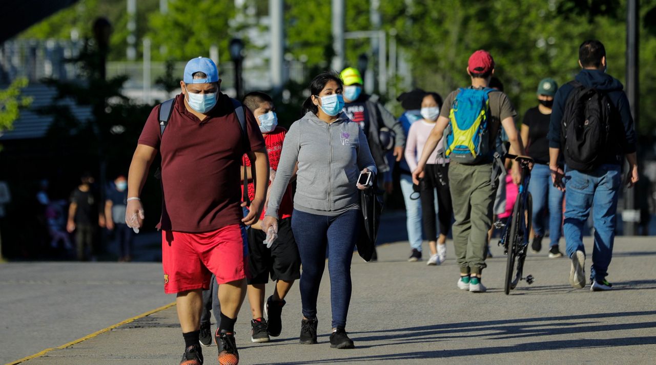Pedestrians wear protective masks during the coronavirus pandemic as they enjoy warm weather in Flushing Meadows Corona Park, Tuesday, May 26, 2020, in the Queens borough of New York. (AP Photo/Frank Franklin II)