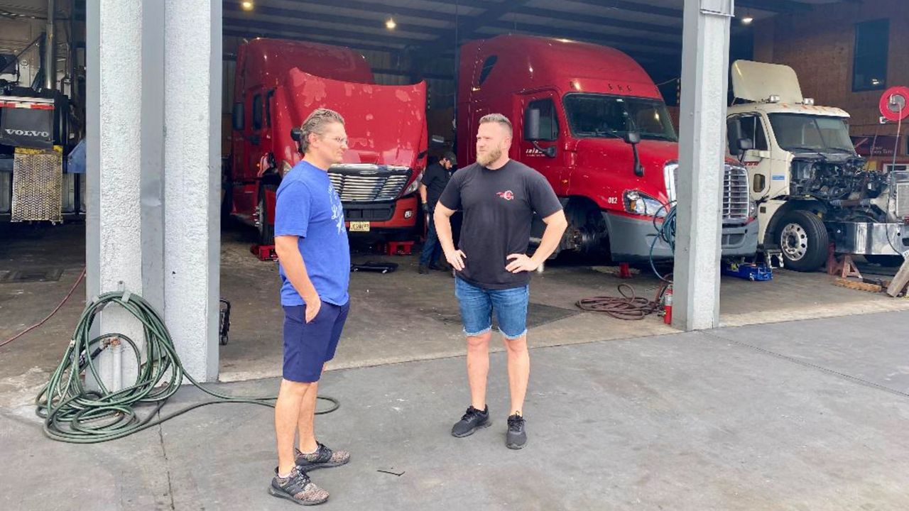 Inland Transport owner Stan Rudnitsky (left) talks with employee Bob Tkachuk, who handles driver recruitment, among other duties, in front of the company's repair shop. (Spectrum News/Pete Reinwald)