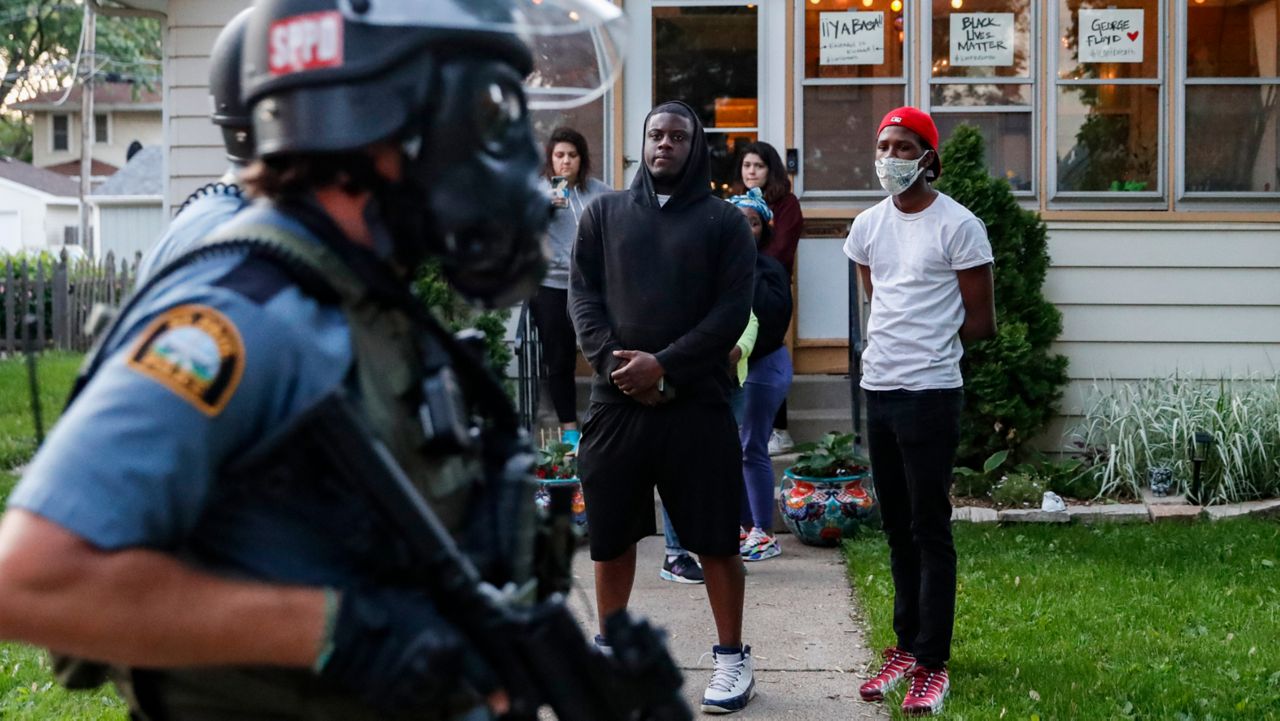 Residents protesting the death of George Floyd watch police in riot gear walk down a street Thursday, May 28, 2020, in St. Paul, Minnesota. (John Minchillo/AP)