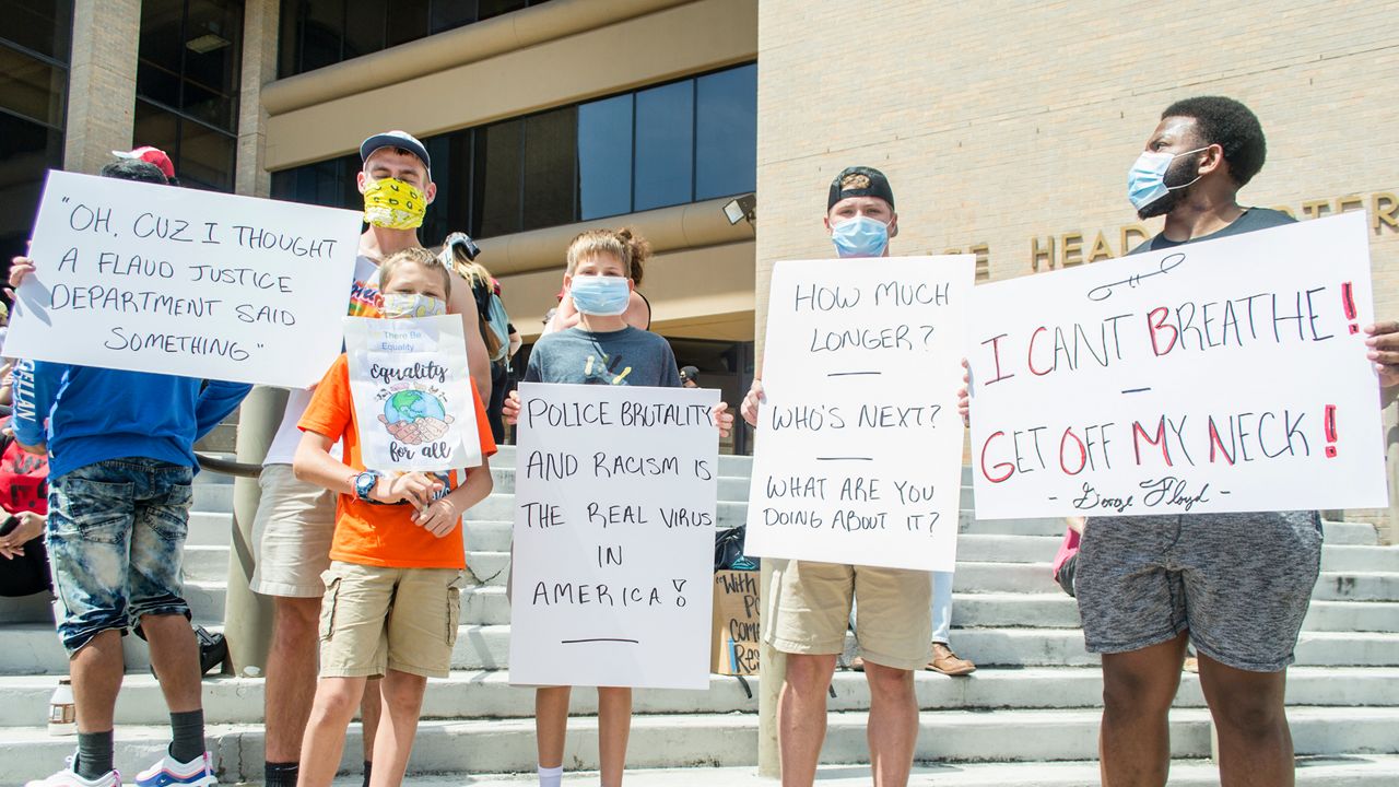 People hold signs in front of APD headquarters.