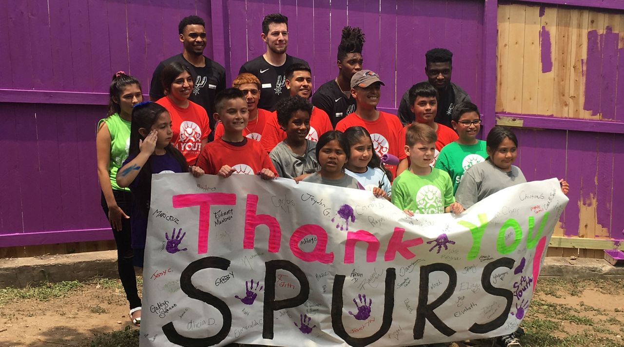 Ben Moore, Drew Eubanks, Lonnie Walker IV and Chimezie Metu take picture with kids at SA Youth with a handmade "thank you" post May 30, 2019 (Spectrum News)