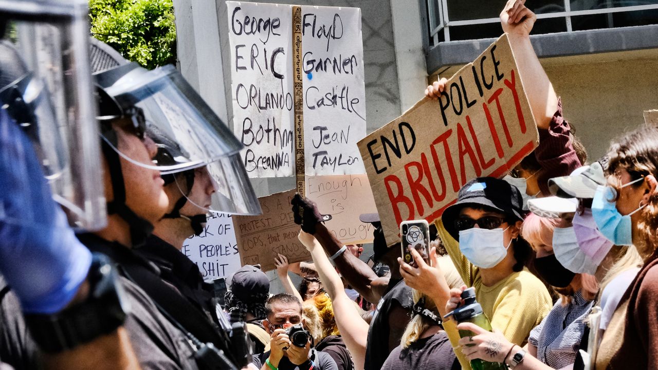 In this Sunday May 31, 2020 photo protesters hold signs and chant slogans while facing off with Santa Monica police during a Black Lives Matter protest. (AP Photo/Richard Vogel)