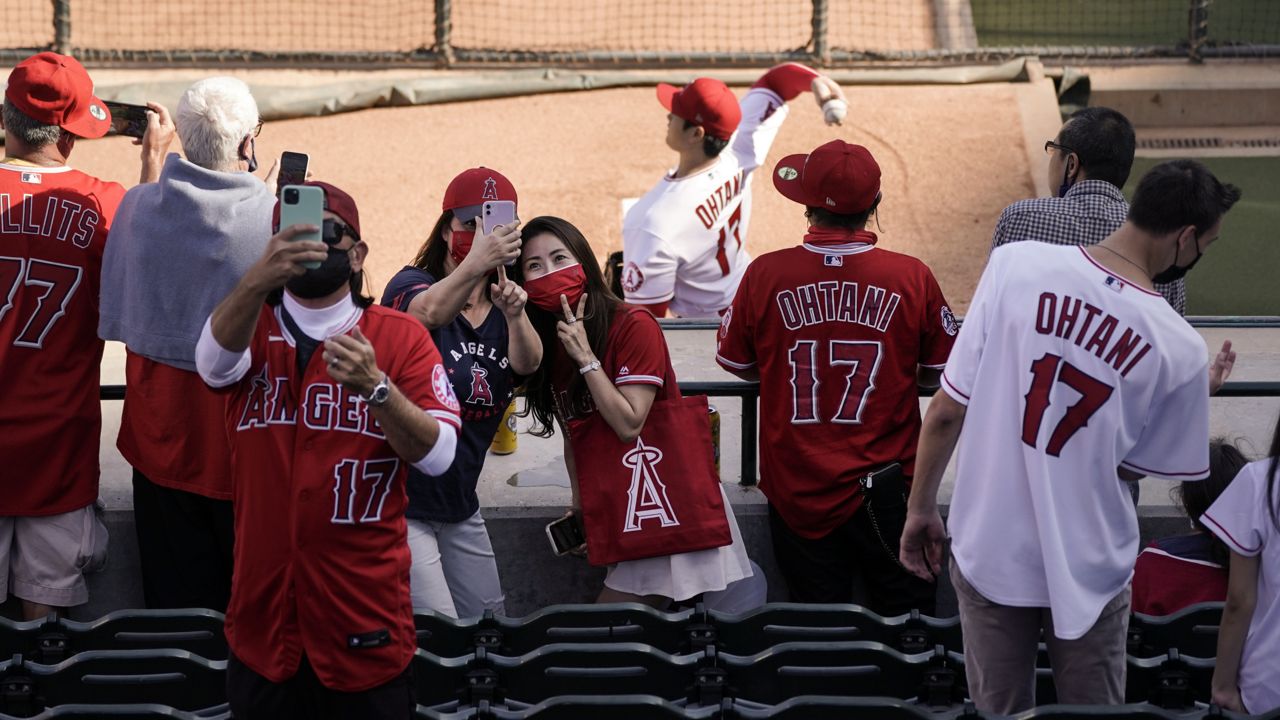 Fans take a selfie as Los Angeles Angels starting pitcher Shohei Ohtani, of Japan, warms up in the bullpen before the team's baseball game against the Cleveland Indians, Wednesday, May 19, 2021, in Anaheim, Calif. (AP Photo/Jae C. Hong)