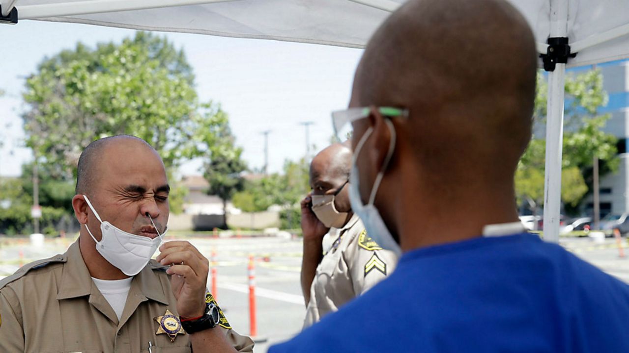 Los Angeles County Sheriff Paul Heang, left, takes a COVID-19 test Monday, April 27, 2020, in Carson, Calif. The CDC will release new priorities for coronavirus testing Monday, including testing asymptomatic individuals in high-risk settings. (AP Photo/Marcio Jose Sanchez)