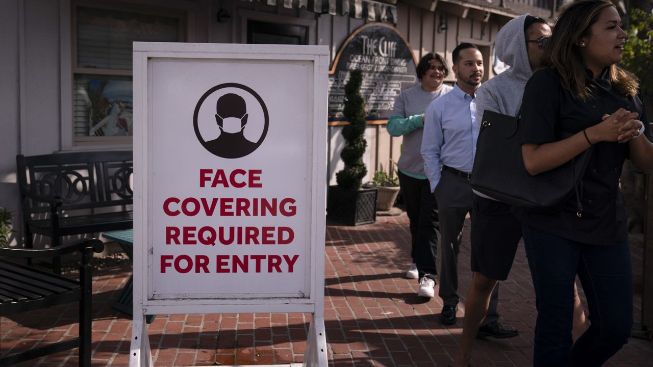 People walk past a sign requesting customers to wear masks in Laguna Beach, Calif., Monday, May 17, 2021. (AP Photo/Jae C. Hong)