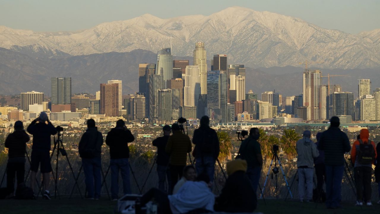 People take photos of snow covered mountains behind the downtown Los Angeles skyline Tuesday, Dec. 29, 2020, in Los Angeles. (AP Photo/Ashley Landis)