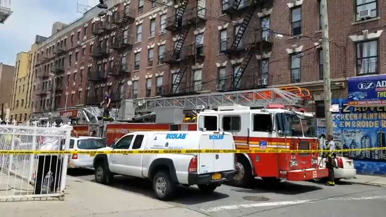 A mini-van, left, and an FDNY fire truck, right, about three feet apart, parked near a pole near a red-brick building. Yellow police tape is about ten feet in front of the vehicles.