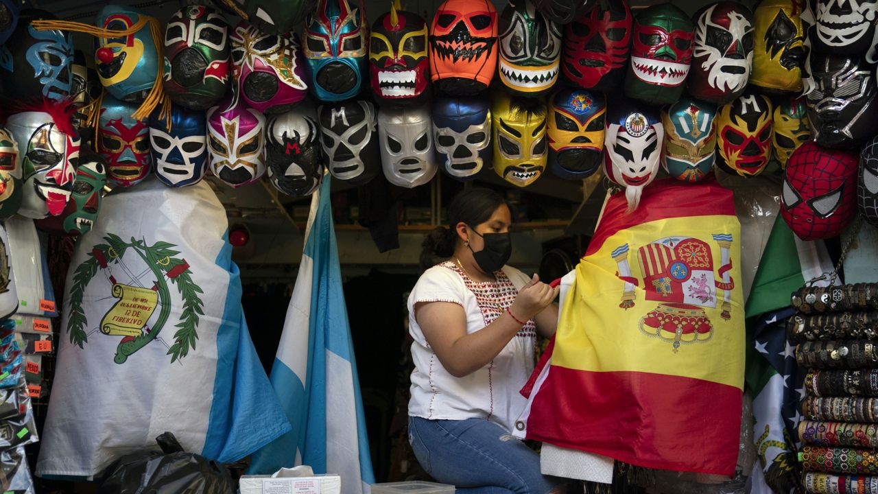 Clerk Wendy Ramirez uses a Spanish flag to wrap souvenirs while preparing to close the store for the day on Olvera Street in Los Angeles, Tuesday, June 8, 2021. (AP Photo/Jae C. Hong)