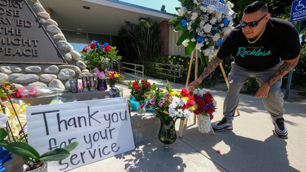 A man places flowers at a memorial Wednesday outside El Monte City Hall for two police officers who were shot and killed Tuesday, at a motel in El Monte, Calif. (AP Photo/Ringo H.W. Chiu)