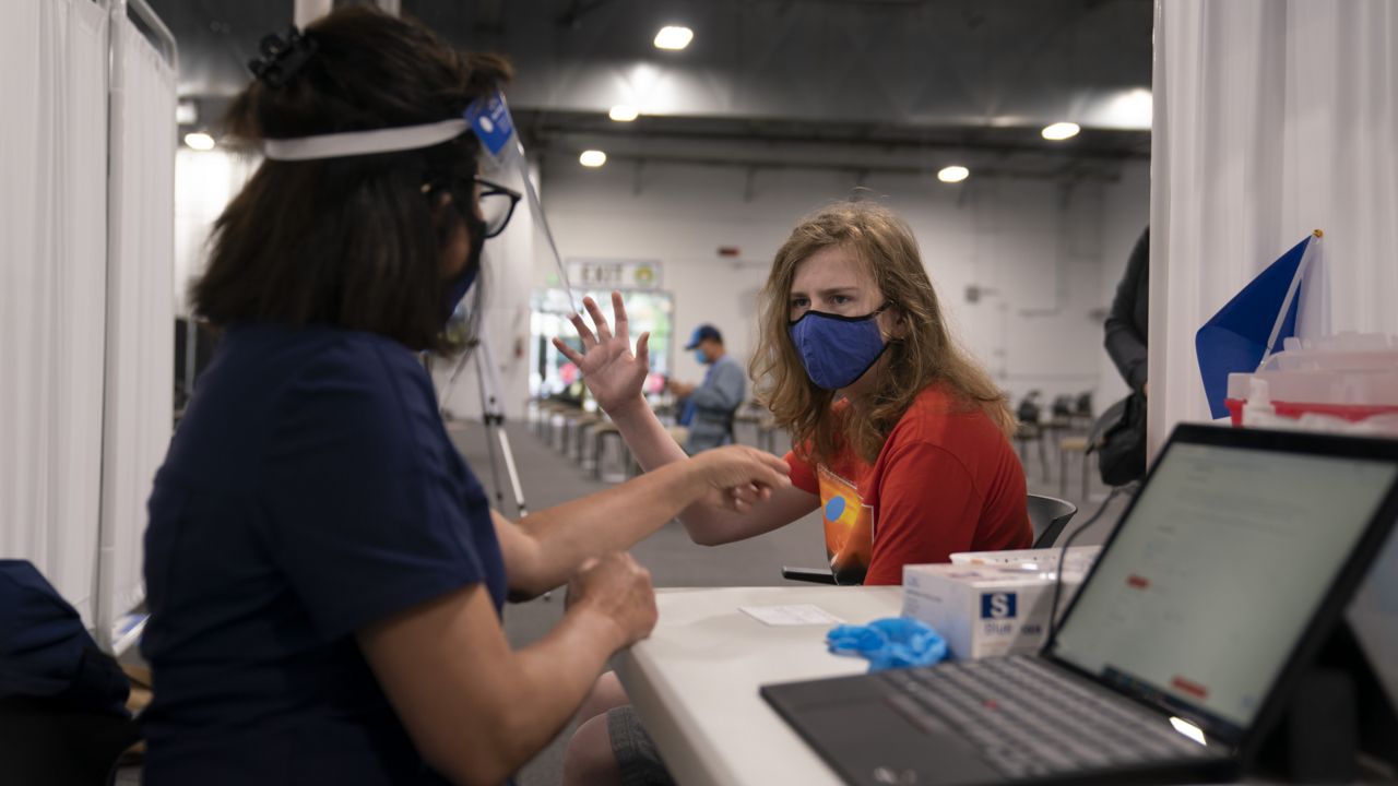 Garrette Parkison, 14, raises his writing hand as registered nurse Anna Ehrlich prepares to administer a dose of the Pfizer COVID-19 vaccine at Providence Edwards Lifesciences vaccination site in Santa Ana, Calif., Thursday, May 13, 2021. (AP Photo/Jae C. Hong)