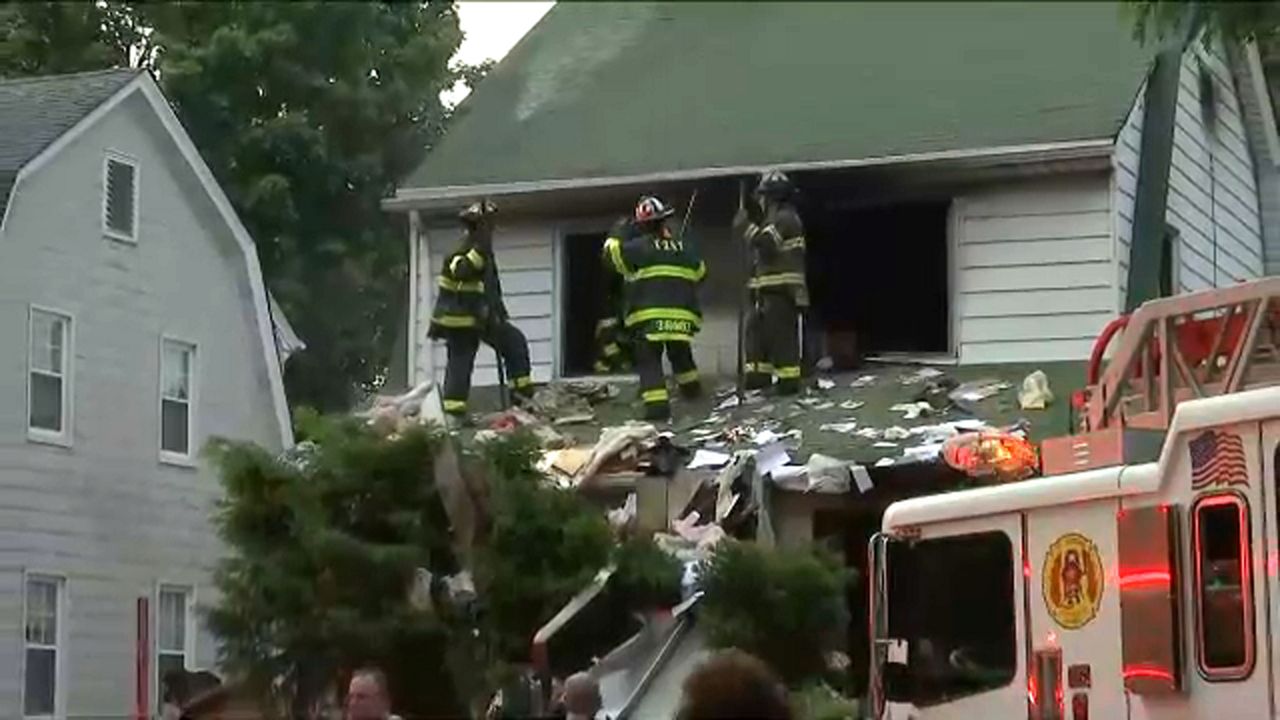 Three people wearing FDNY uniforms stand near the roof a house.
