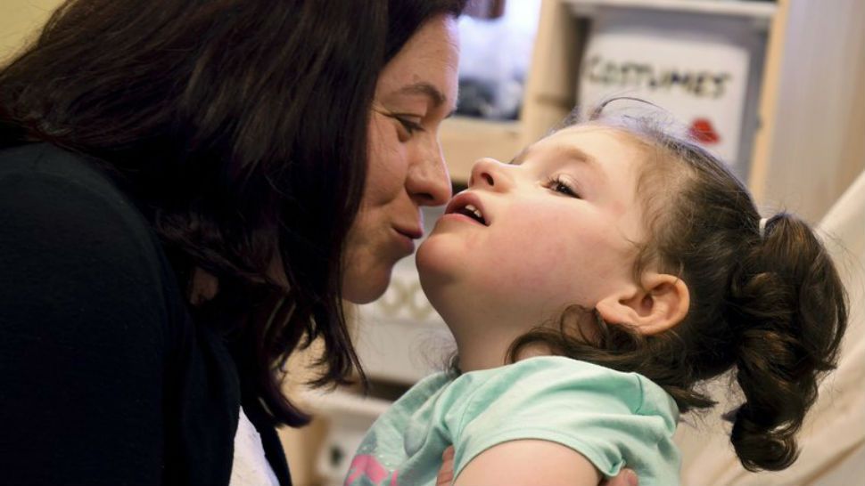 In this April 23, 2018, photo, Meagan Patrick kisses her daughter, Addelyn Patrick, 5, in the playroom at Realm of Caring in Colorado Springs, Colo. Addelyn was born with a brain malformation and suffers from multiple forms of seizures. The U.S. Food and Drug Administration is expected to decide soon whether to give its first approval to a prescription drug made from the marijuana plant. But parents, including Meagan, who have used other products containing chemicals from the plant to treat their children’s severe forms of epilepsy are feeling more cautious than celebratory. (AP Photo/Thomas Peipert)