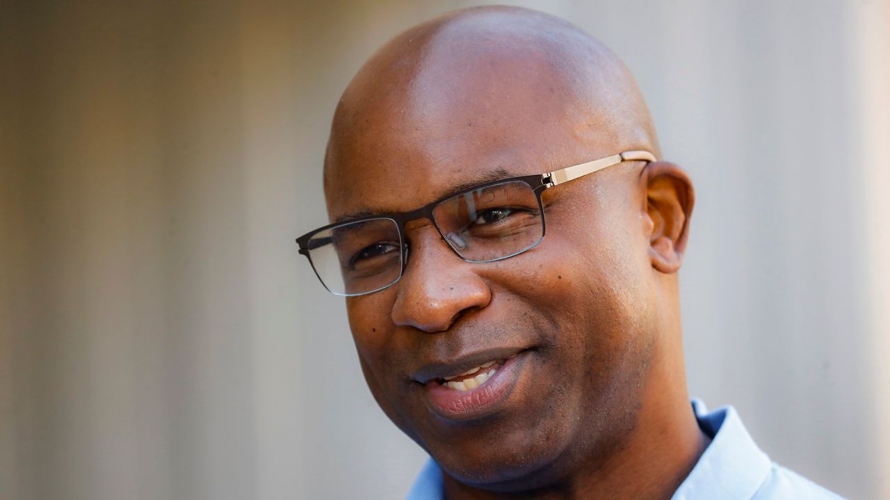 Rep. Jamaal Bowman, wearing black, square glasses and a sky blue dress shirt, in front of a pale background.
