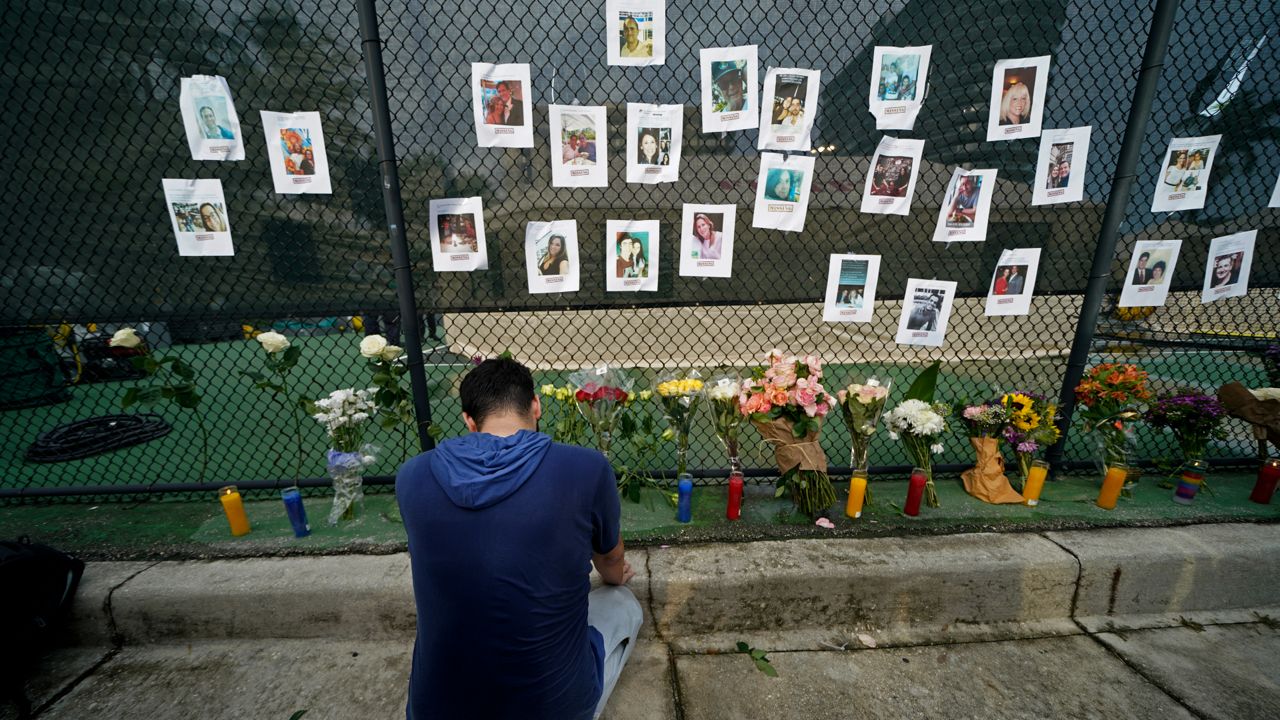 Leo Soto, who created this memorial with grocery stores donating flowers and candles, pauses in front of photos of some of the missing people that he put on a fence, near the site of an oceanfront condo building that partially collapsed in Surfside, Fla., Friday, June 25, 2021. (AP Photo/Gerald Herbert)