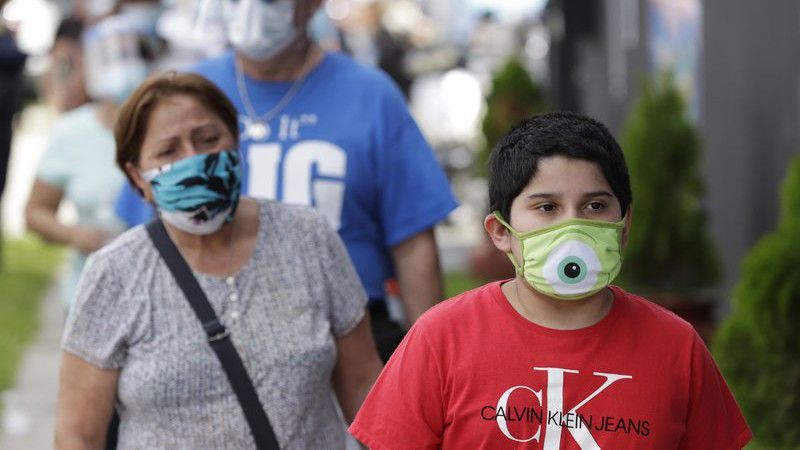 People, social distancing and wearing masks to prevent the spread of the new coronavirus, wait in line at a mask distribution event, Friday, June 26, 2020, in a COVID-19 hotspot of the Little Havana neighborhood of Miami. Florida banned alcohol consumption at its bars Friday as its daily confirmed coronavirus cases neared 9,000, a new record that is almost double the previous mark set just two days ago. (AP Photo/Wilfredo Lee)